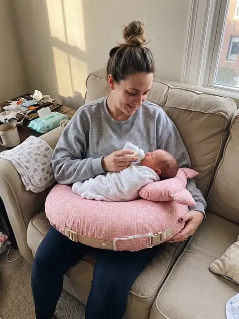 A mother bottle feeding her baby resting on the pillow, her arms relaxed